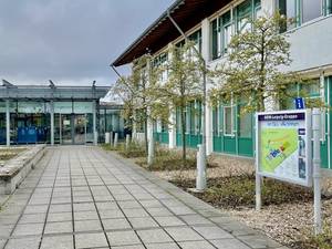 Außenansicht des BBW Leipzig mit gepflastertem Weg, Bäumen und Informationsschild.